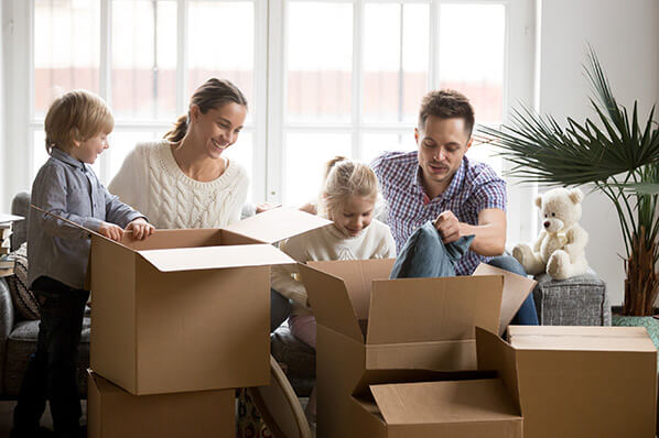 parents with a young girl and a young boy unpacking moving boxes in their new living room