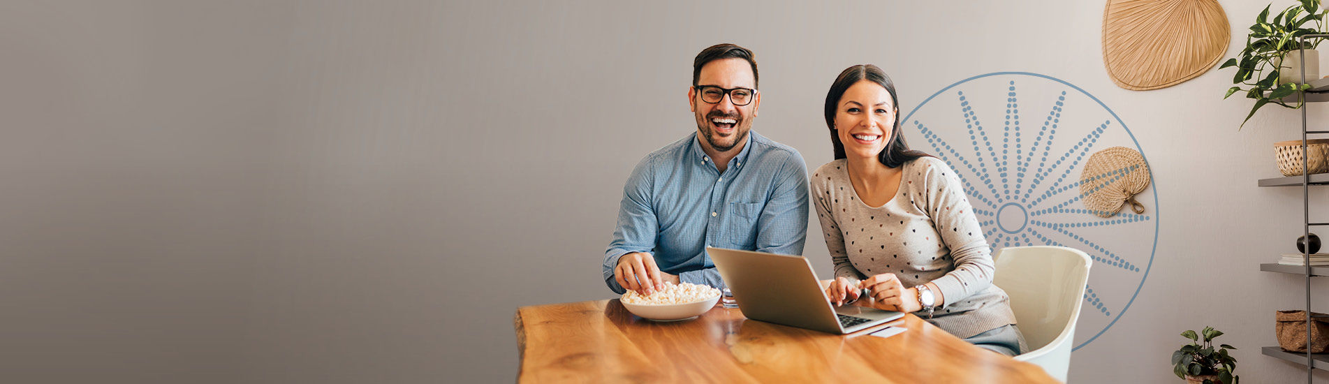 smiling couple sitting at the table looking at their laptop