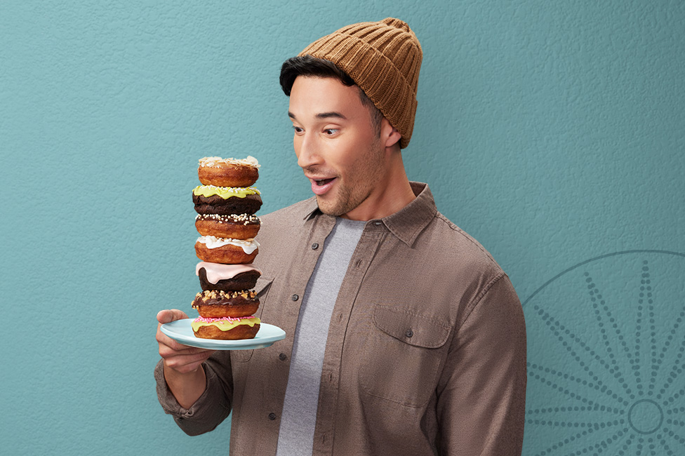 happy young man in a toque holding a plate stacked high with donuts