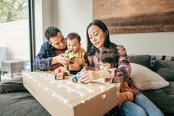 young parents playing with their young children with wooden car toys on a pretend race track