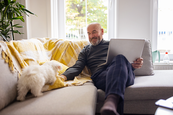 older man sitting on his couch with his little white dog