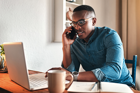 young black man chatting on his phone looking at his laptop