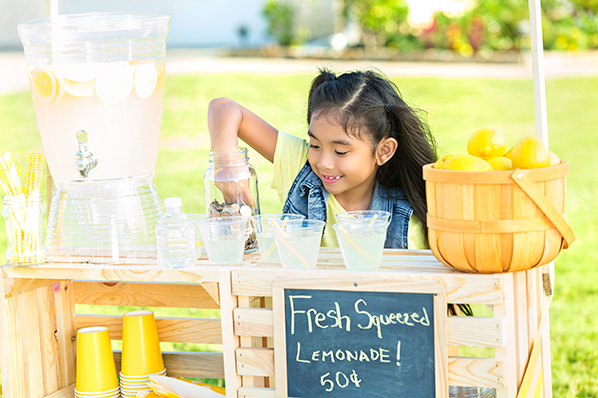 young girl at her lemonade stand reaching in to a mason jar of her earnings