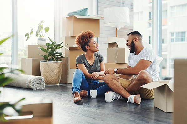 young couple sitting on the floor of their new home amongst all their moving boxes