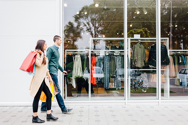 young couple walking in front of a clothing store with shopping bags in hand