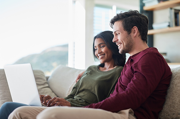 young couple sitting on their living room couch and looking at their laptop