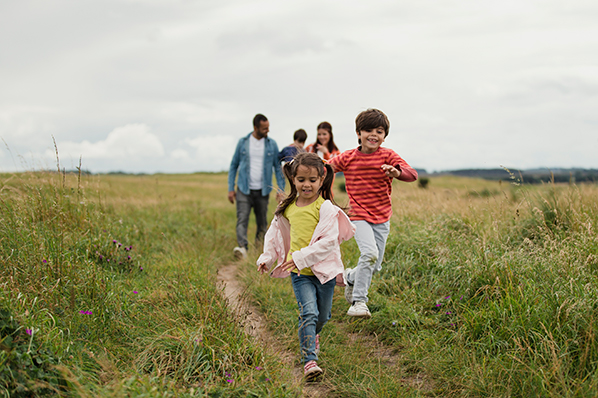 young family out for a walk outdoors with two of their children running ahead of everyone