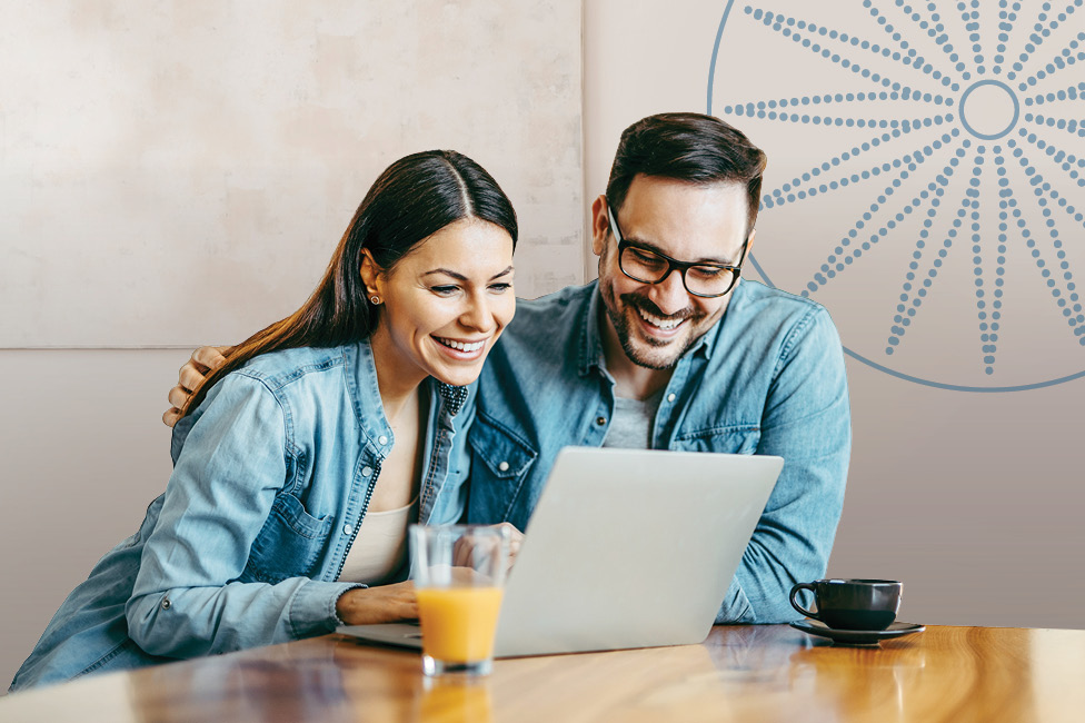 smiling couple sitting at the table looking at their laptop