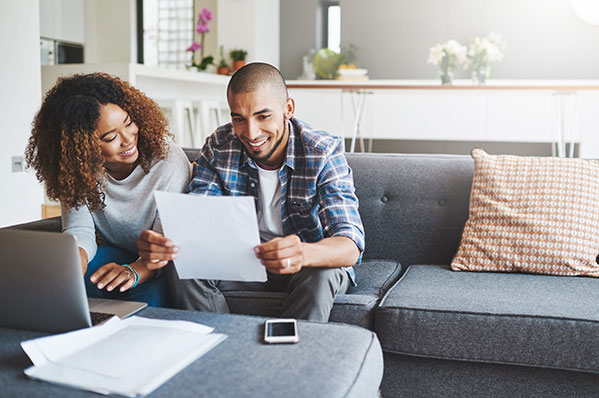 young couple sitting on couch laughing looking at a piece of paper