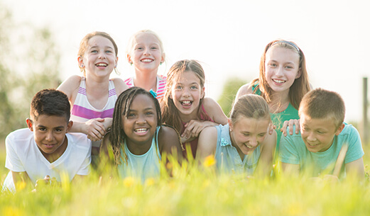 8 young kids lying in the grass smiling at the camera
