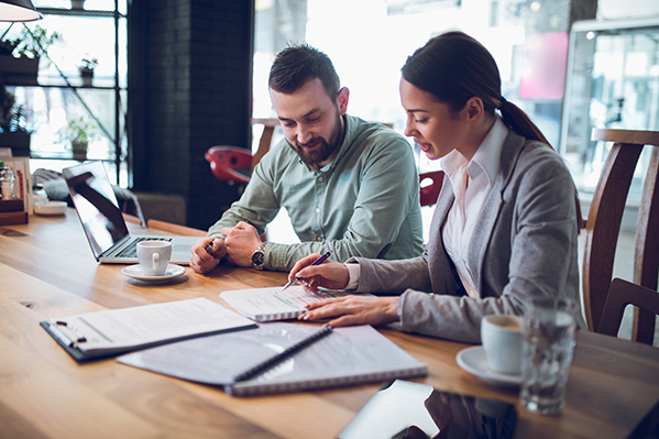 middle-aged male in a dress shirt sitting at a table with a young female advisor looking at different documents.png