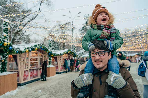 dad walking around a christmas market with a small child on his shoulders