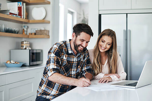 young couple sitting at the kitchen counter looking at documents and their laptop